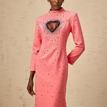 Young woman wearing a long pink maxi dress with heart shaped cutouts and embellishments standing in a neutral background