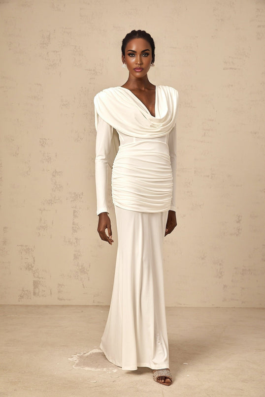 Young woman wearing a long white fitted maxi dress with ruched detailing standing against a plain background