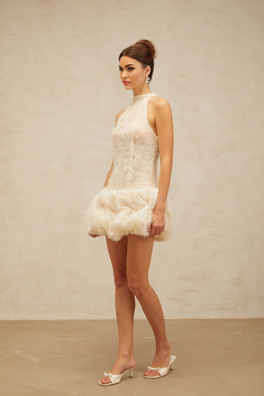 Young woman wearing a neutral beige textured mini dress with puff sleeves standing against a plain background