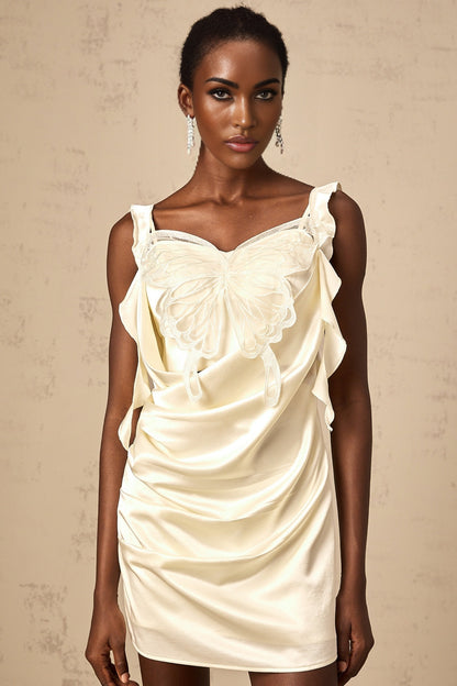 Young woman wearing a neutral colored mini dress with butterfly print and draped design standing in front of plain background