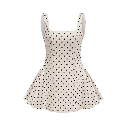 Young woman wearing a neutral colored polka dot mini dress with puff sleeves and a fitted waist standing against a plain background