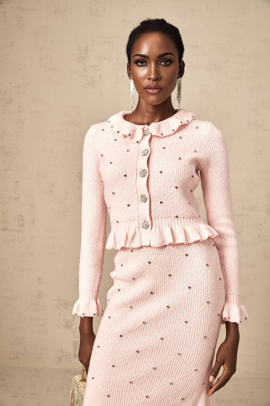 Young woman wearing a pink argyle pattern knitted cardigan and matching skirt set against a plain background