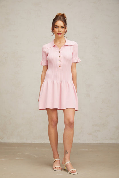 Young woman wearing a pink flared mini dress with fine knit fabric standing against a plain background