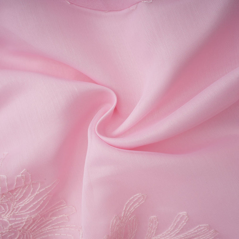Young woman wearing a pink mini dress with floral embroidery and layered skirt standing in a casual pose against a plain background