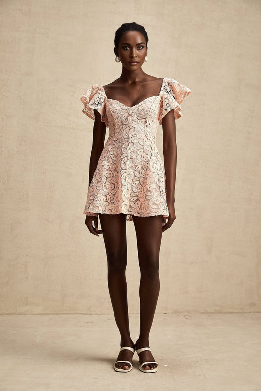 Young woman wearing a pink mini dress with flutter sleeves and lace detailing standing in a relaxed pose against a plain background