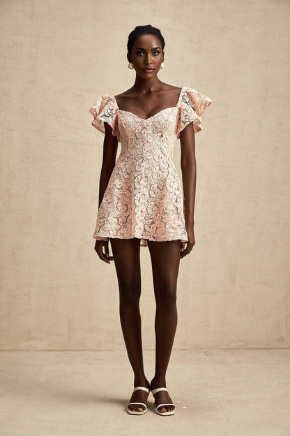 Young woman wearing a pink mini dress with flutter sleeves and lace detailing standing in a relaxed pose against a plain background