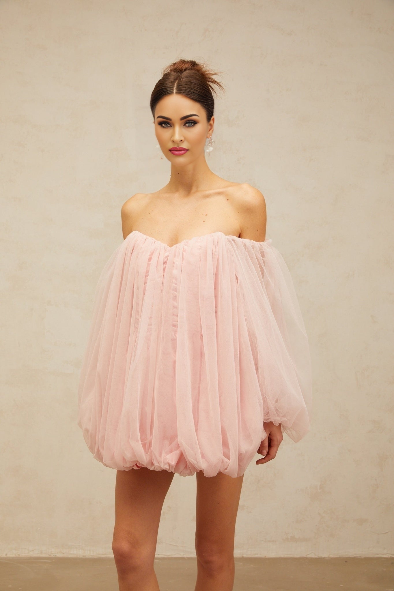 Young woman wearing a pink mini dress with layered bubble tulle skirt standing against a plain background