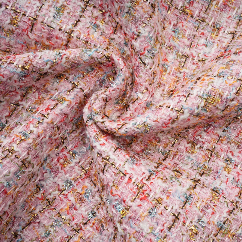 Young woman wearing a pink tweed mini dress with embellishments standing against a plain background