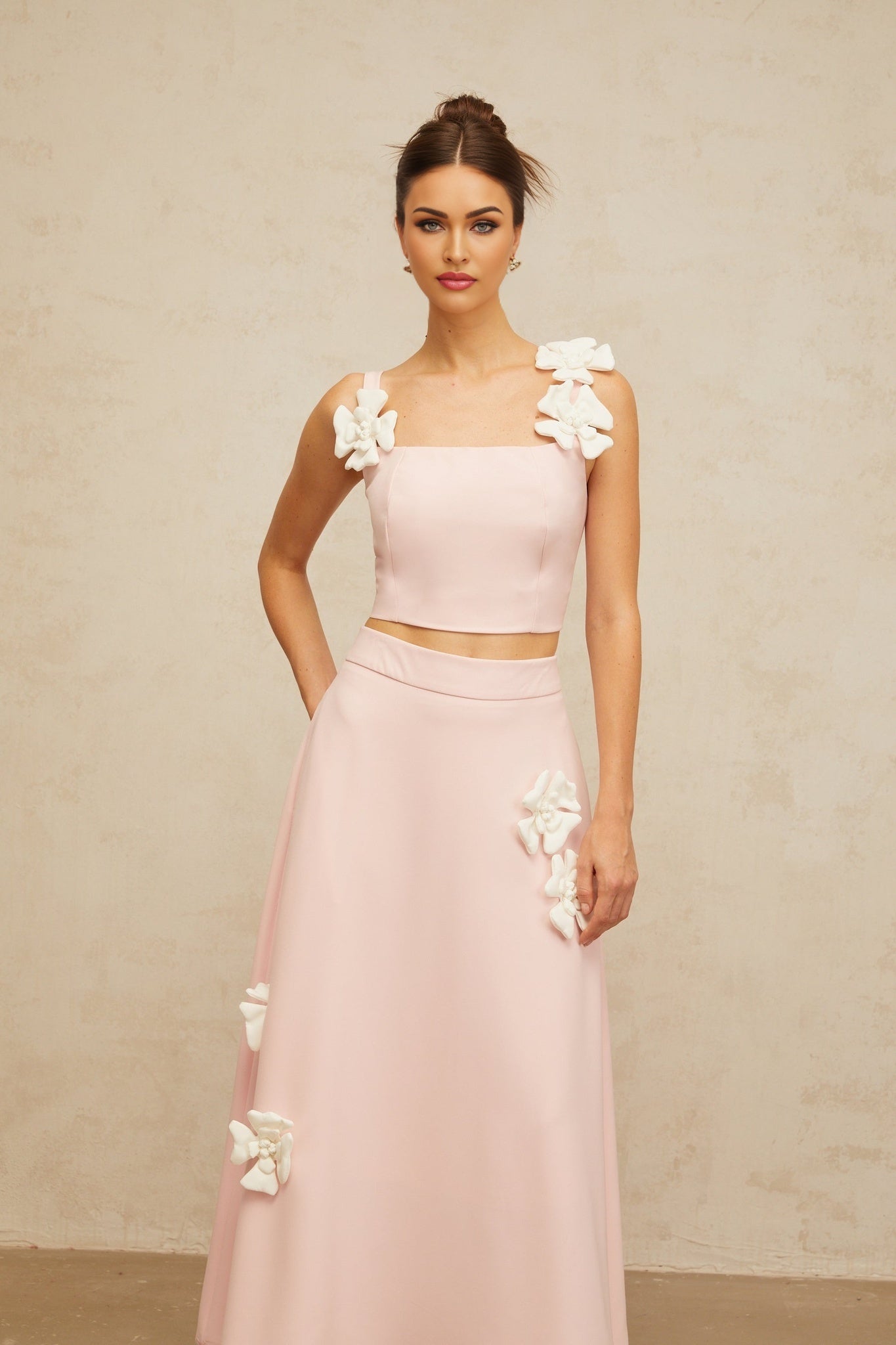 Young woman wearing a pink twopiece outfit with floral applique details consisting of a cropped top and matching skirt