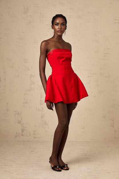 Young woman wearing a red off shoulder flared mini dress with short sleeves standing against a plain background