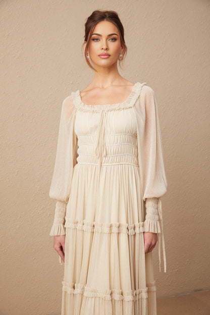 Young woman wearing a shimmering gold pleated midi dress with shirred detailing and short sleeves standing in front of a plain background