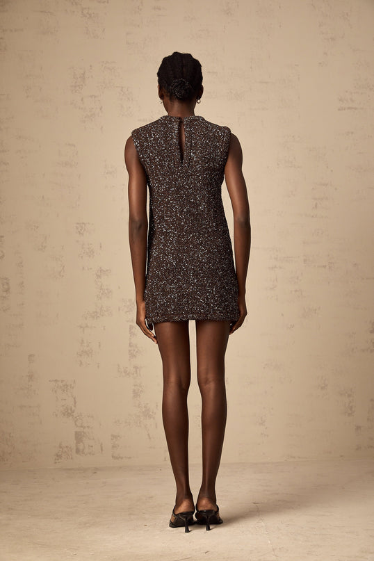 Young woman wearing a short barleybrown knit dress with allover sequin embellishment and formfitting silhouette