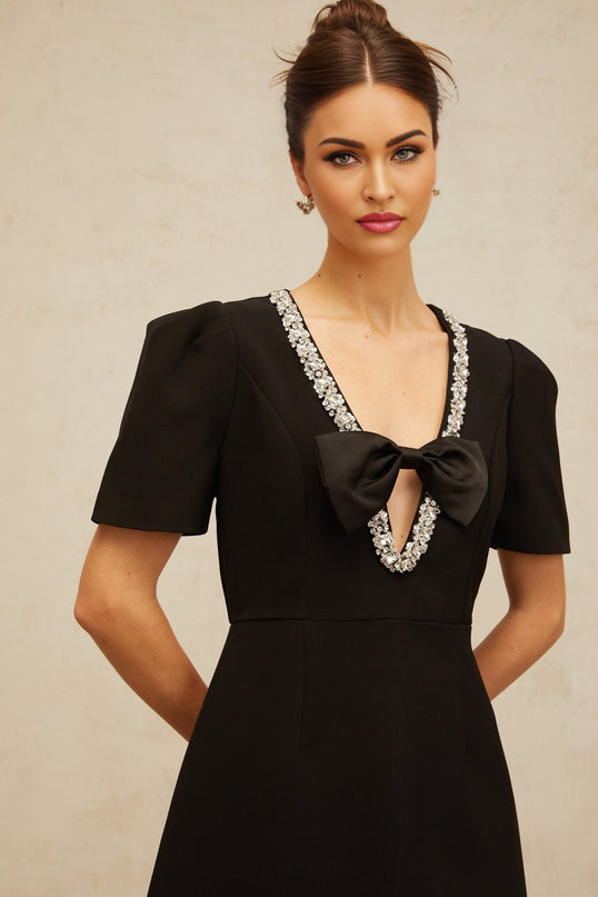Young woman wearing a short black dress with a large bow detail