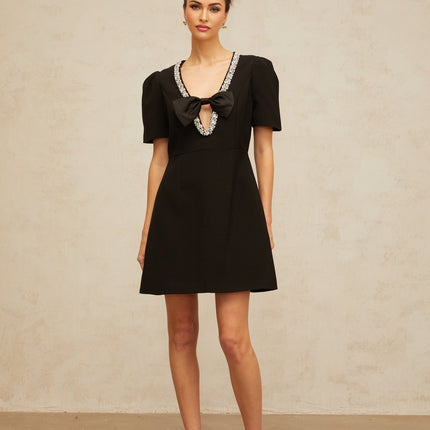 Young woman wearing a short black dress with a large decorative bow detail