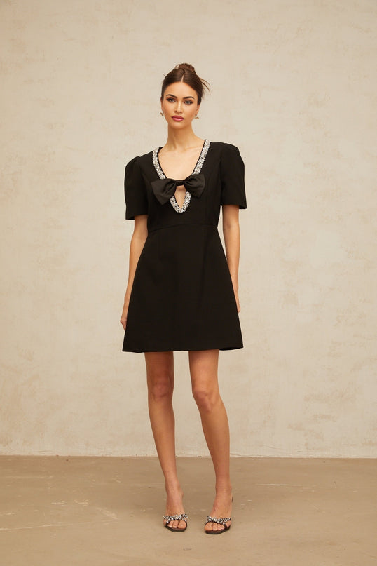Young woman wearing a short black dress with a large decorative bow detail