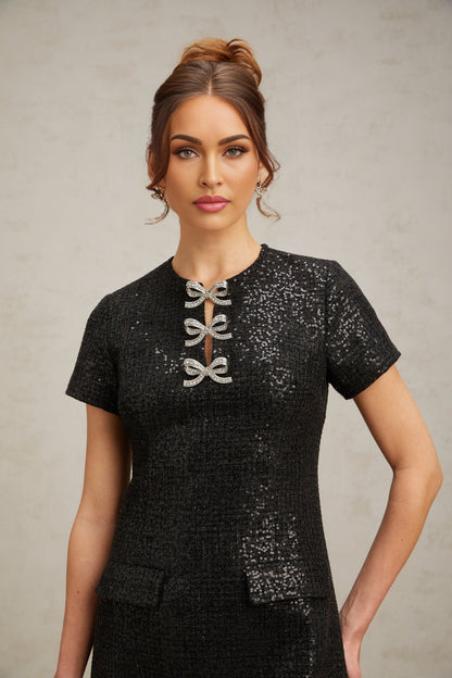 Young woman wearing a short black mini dress with glitter details and thin straps