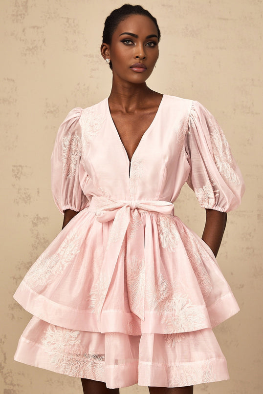 Young woman wearing a short pink dress with floral embroidery and multiple layers standing in a garden setting