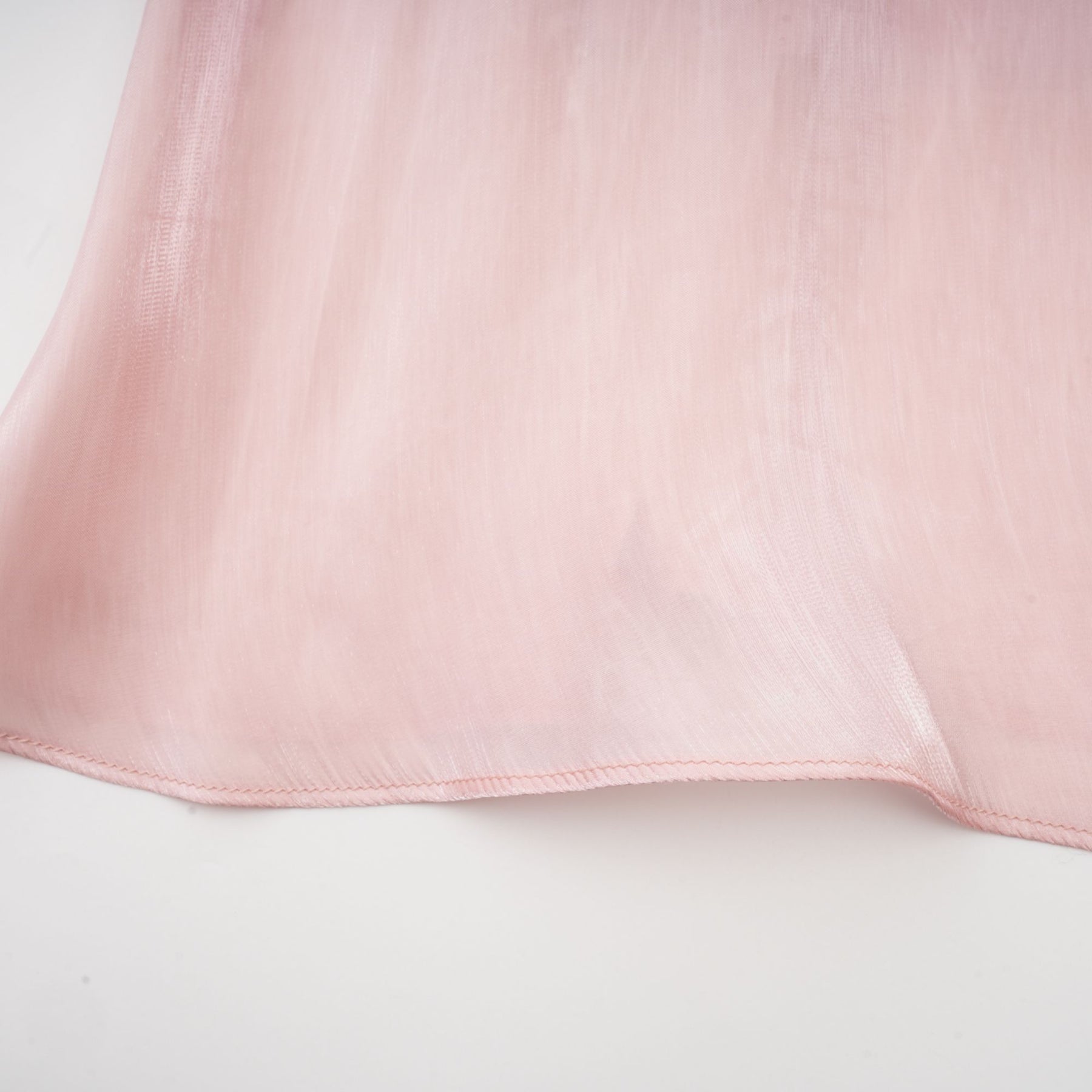 Young woman wearing a short pink dress with pleats and embellishments standing against a plain background