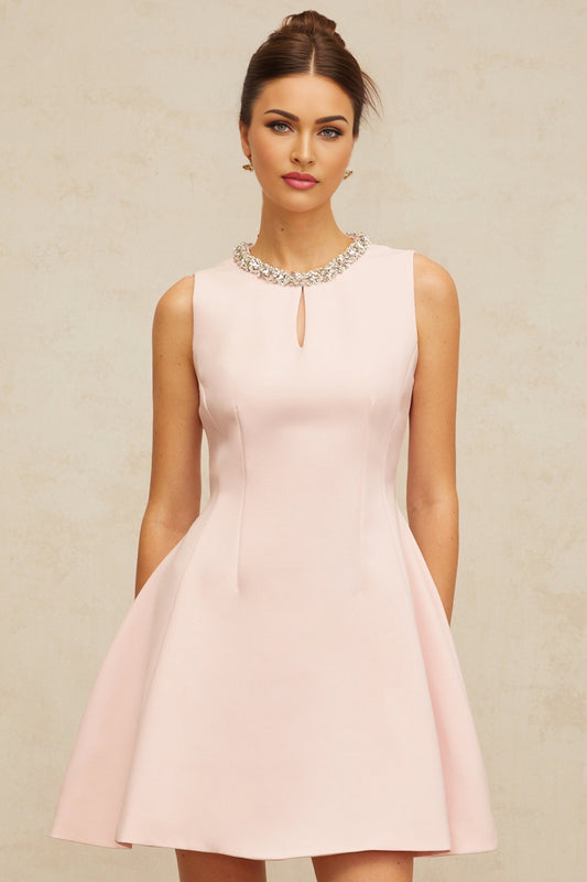 Young woman wearing a short pink dress with sequins and puff sleeves standing against a plain background