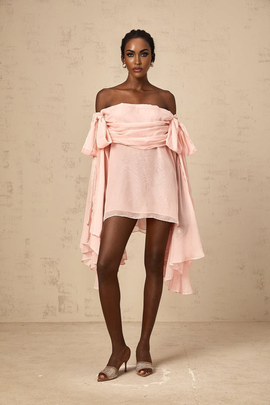 Young woman wearing a short pink mini dress with bow detail and draped fabric design