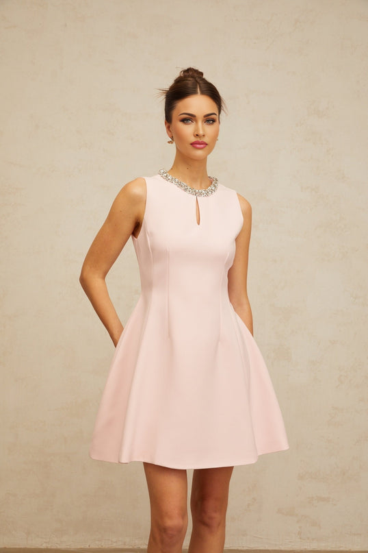 Young woman wearing a short pink mini dress with sequin embellishments and puff sleeves standing against a plain background