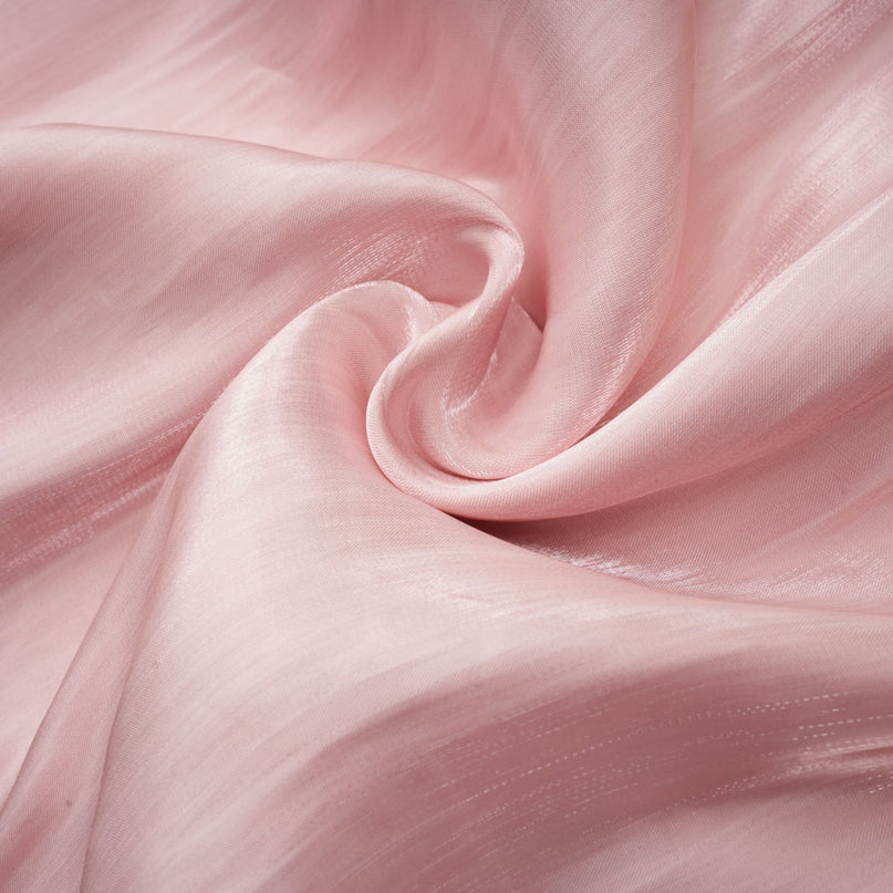 Young woman wearing a short pink pleated dress with embellishments standing against a plain background