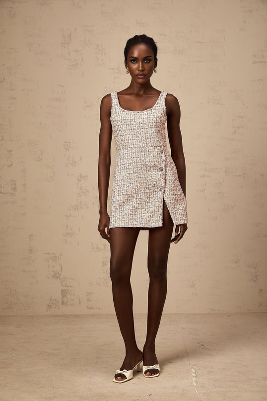 Young woman wearing a short pink tweed dress with sparkly embellishments standing against a plain background