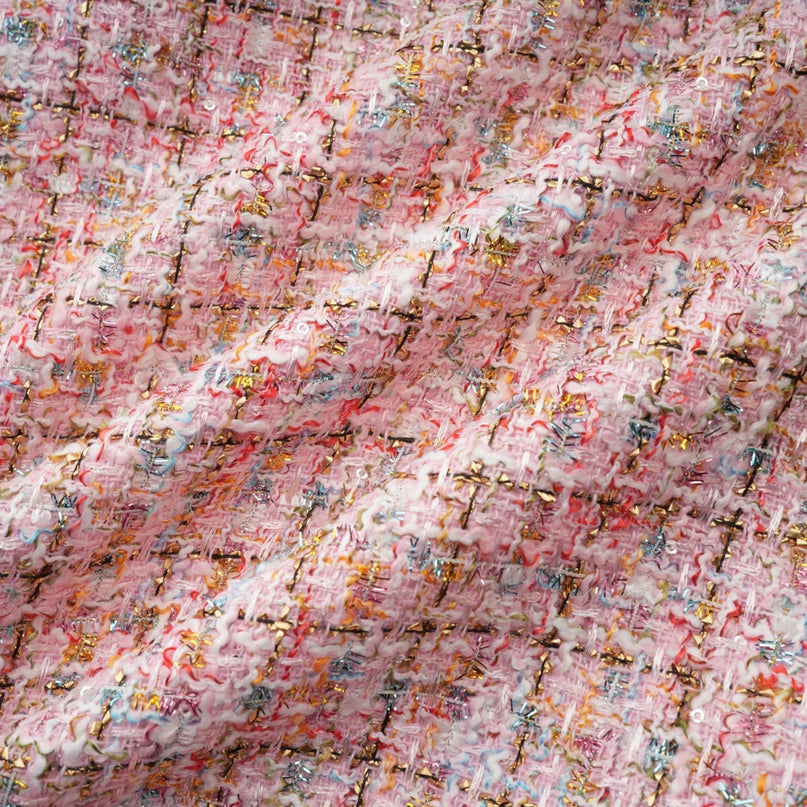 Young woman wearing a short pink tweed dress with sparkly embellishments standing against a plain background