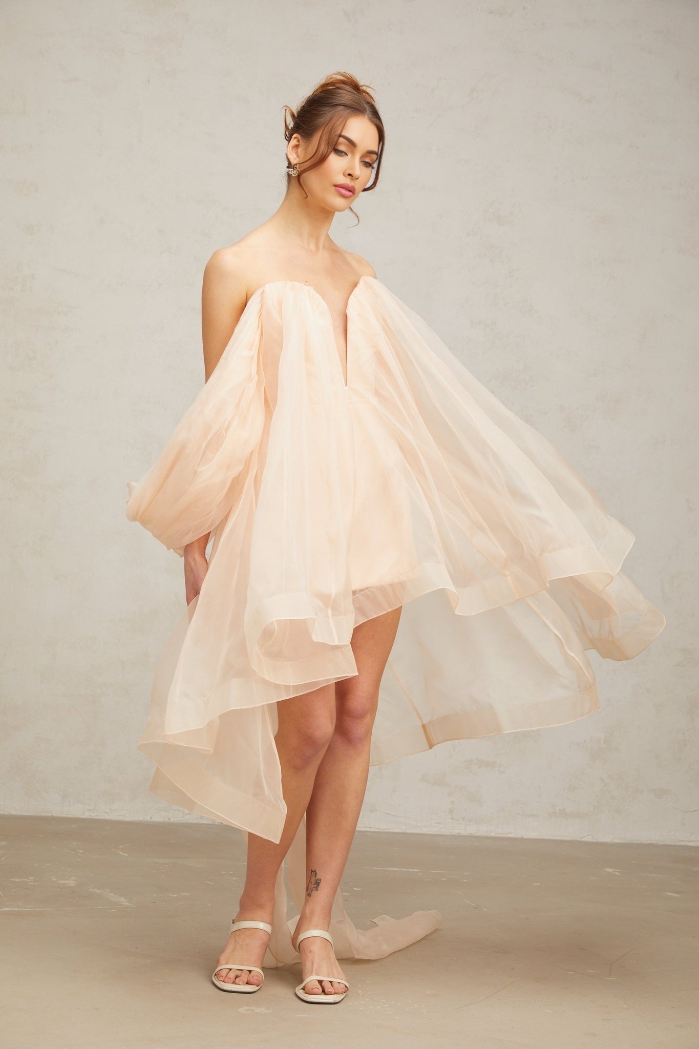 Young woman wearing a short puffy mini dress with large bow detail at the waist and voluminous skirt in a light color