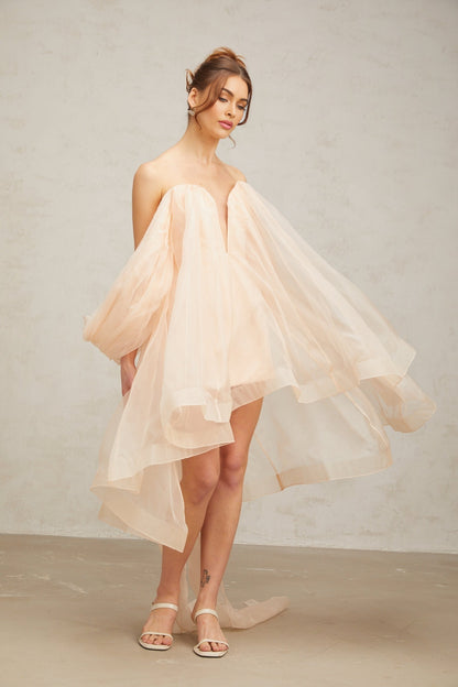 Young woman wearing a short puffy mini dress with large bow detail at the waist and voluminous skirt in a light color