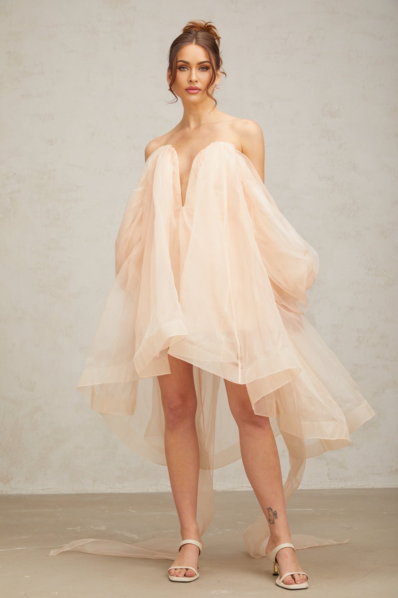 Young woman wearing a short voluminous dress with bow details and puffed sleeves in a light color