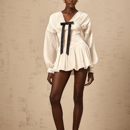 Young woman wearing a short white dress with a bow detail and glitter accents