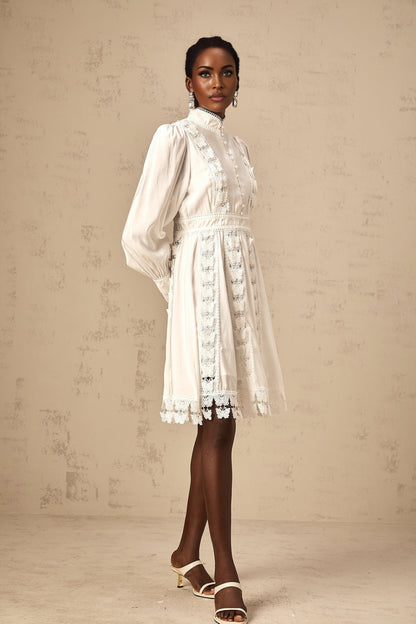 Young woman wearing a short white dress with butterfly appliques standing against a plain background