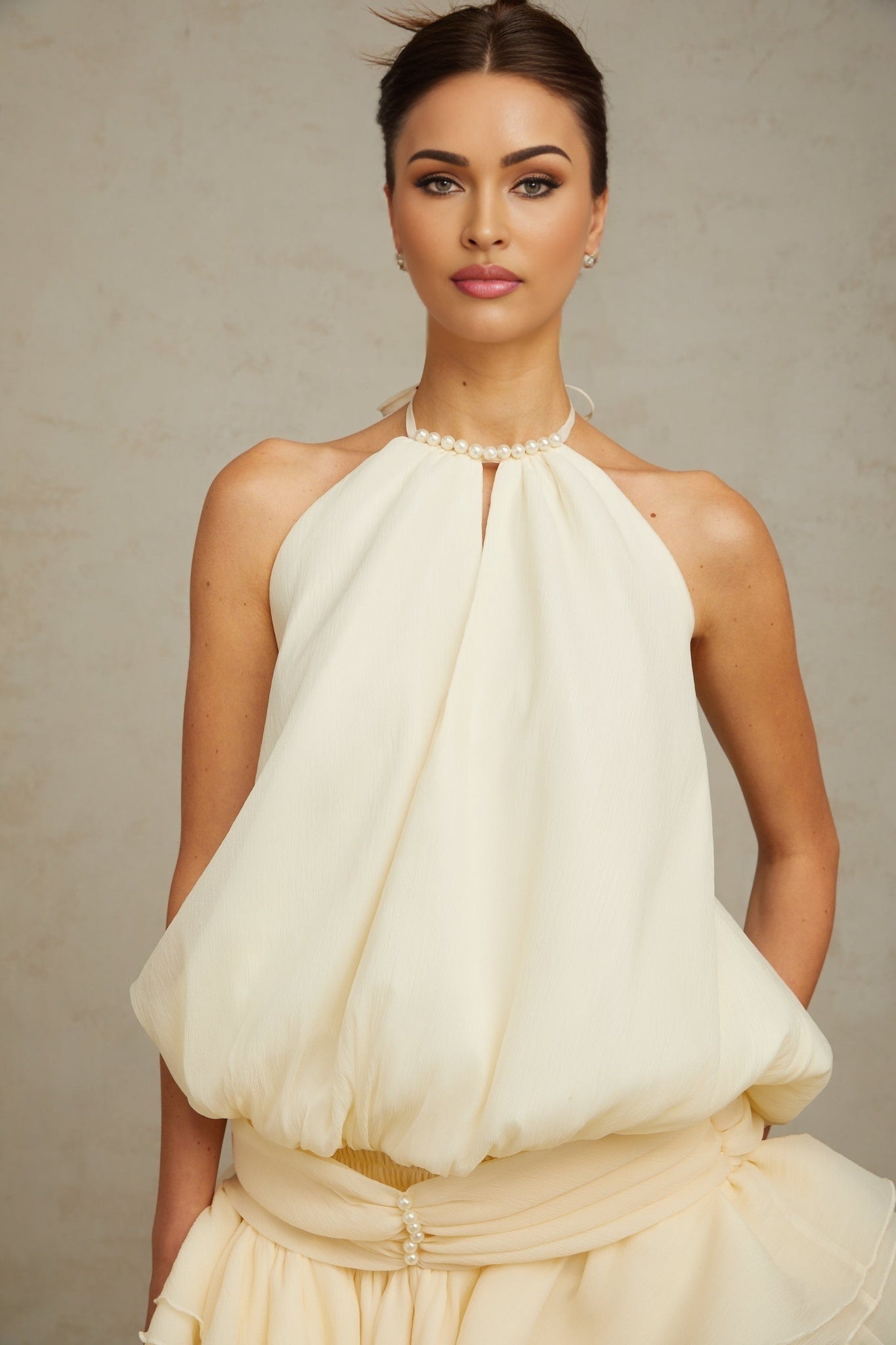 Young woman wearing a short white halterneck dress with faux pearl embellishments