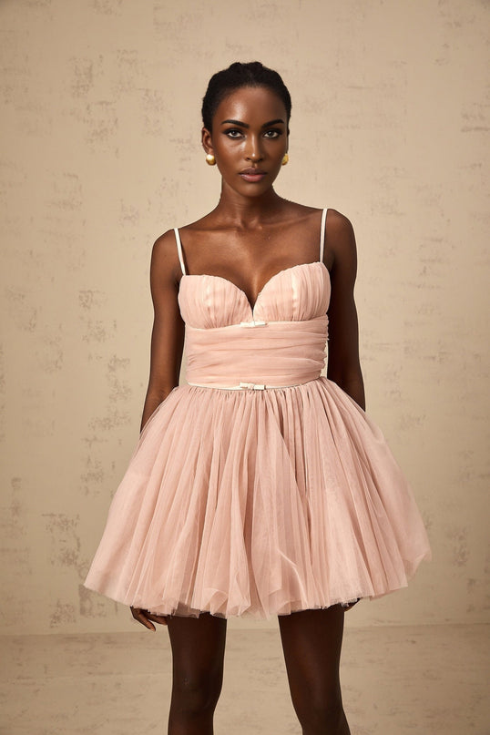 Young woman wearing a sleeveless pleated tulle mini dress in a light color standing in a neutral background