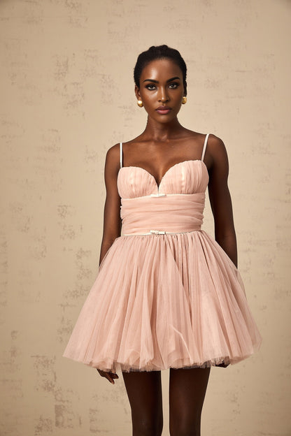 Young woman wearing a sleeveless white mini dress with pleated tulle skirt standing in a studio setting