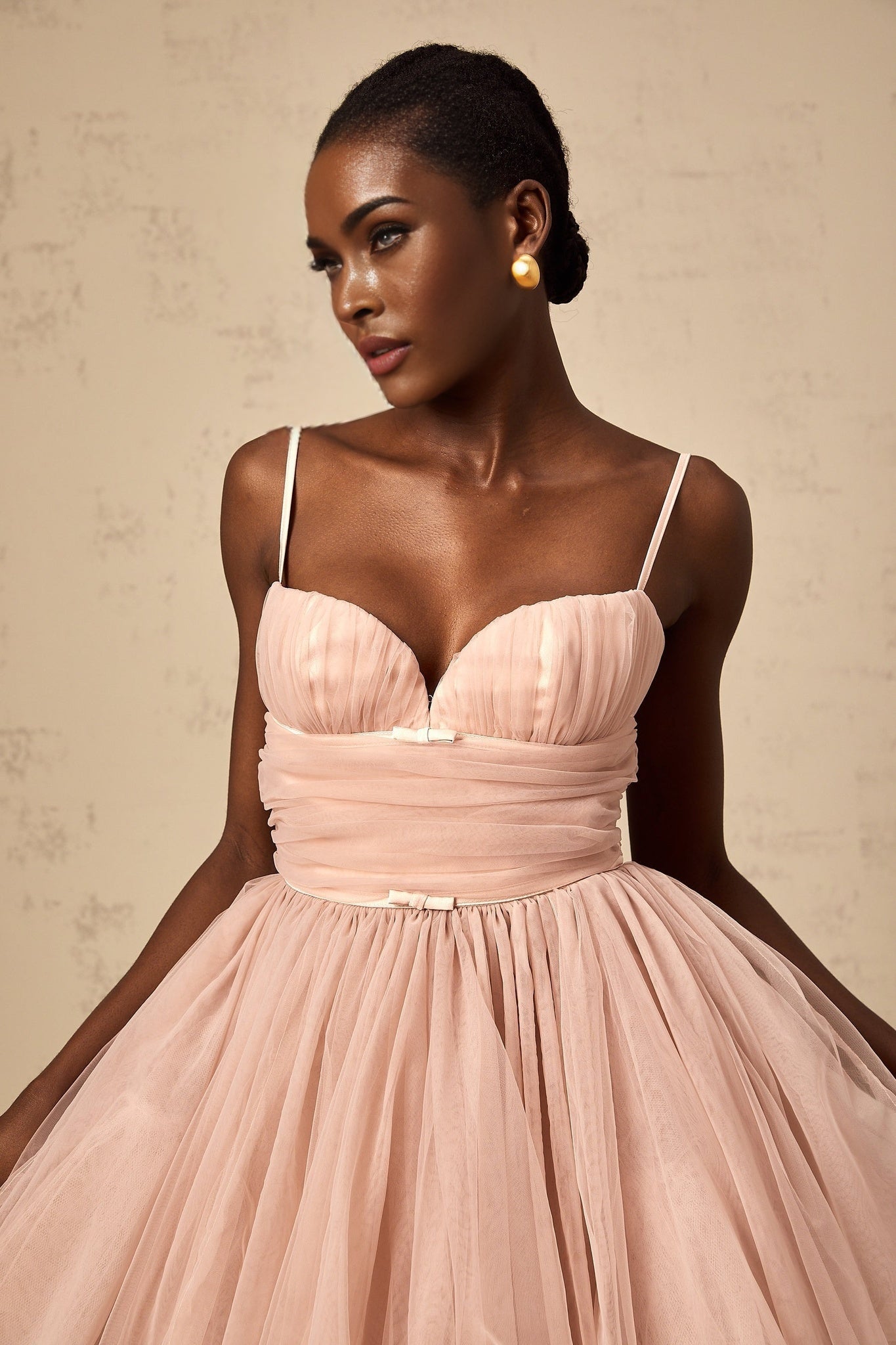 Young woman wearing a sleeveless white tulle mini dress with pleated details and a fitted bodice standing against a plain background