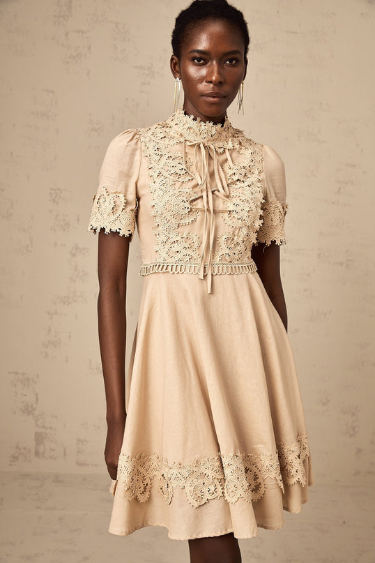 Young woman wearing a white flared mini dress with intricate corded lace pattern and short sleeves posing against a plain background