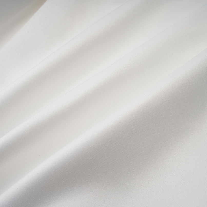 Young woman wearing a white halterneck mini dress with ruffled details standing against a plain background