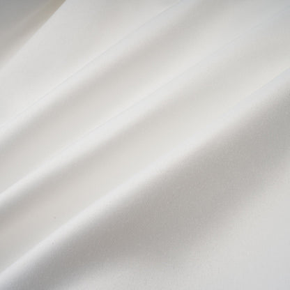 Young woman wearing a white halterneck mini dress with ruffled details standing against a plain background