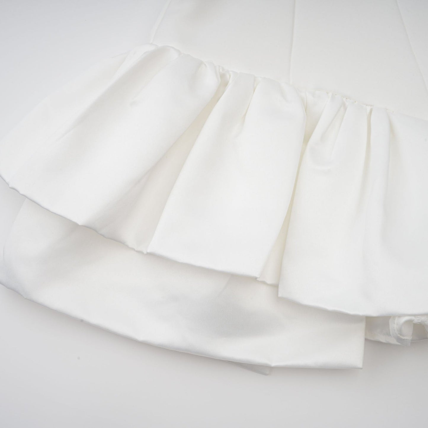 Young woman wearing a white halterneck mini dress with ruffled details standing against a plain background