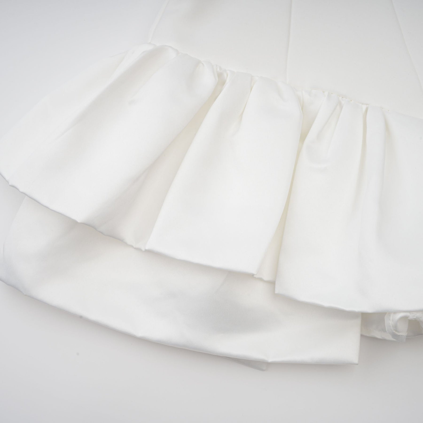 Young woman wearing a white halterneck mini dress with ruffled details standing against a plain background