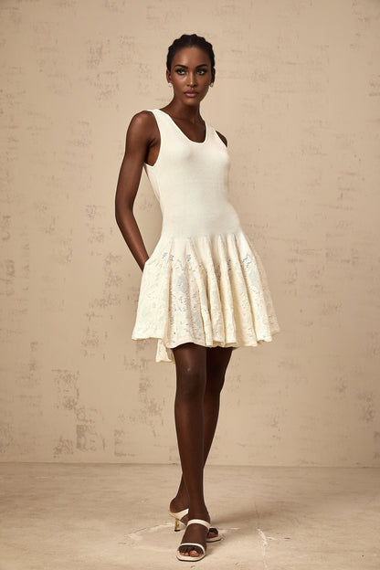 Young woman wearing a white jacquard knit mini dress with textured pattern standing against plain background