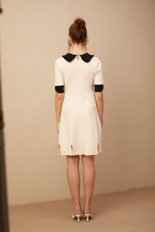 Young woman wearing a white knitted mini dress with split hem detail standing against plain background