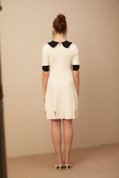 Young woman wearing a white knitted mini dress with split hem detail standing against plain background