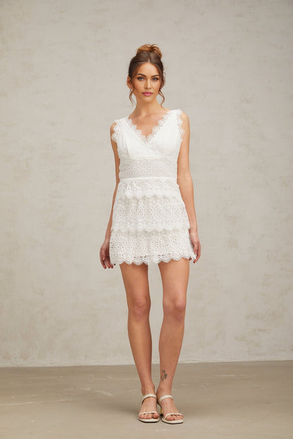 Young woman wearing a white lace tiered mini dress with short sleeves standing against a plain background