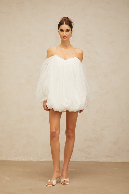 Young woman wearing a white layered bubble tulle mini dress with short puffed sleeves standing against a plain background