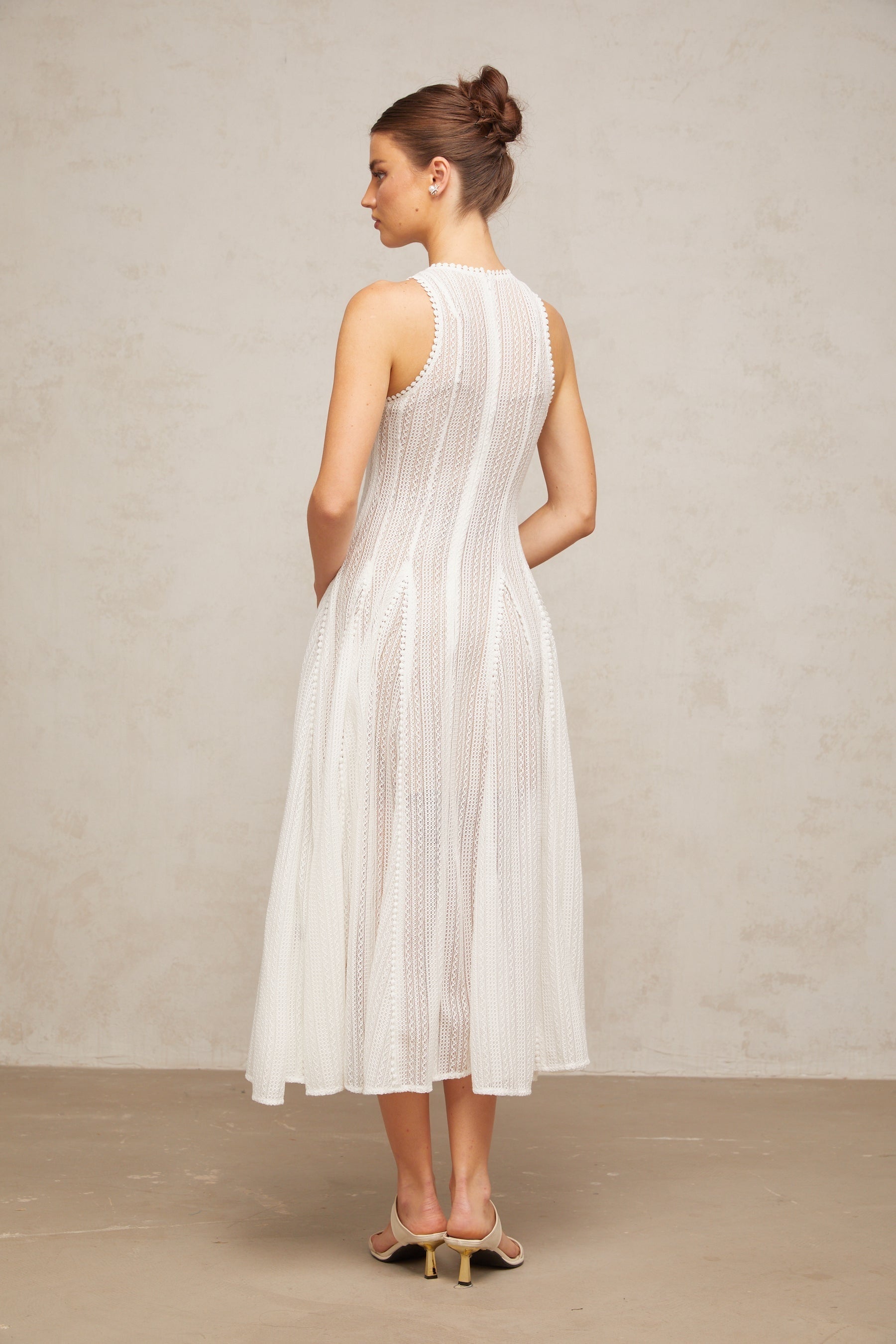 Young woman wearing a white midi dress with pointelle detailing and puff sleeves standing in a neutral background