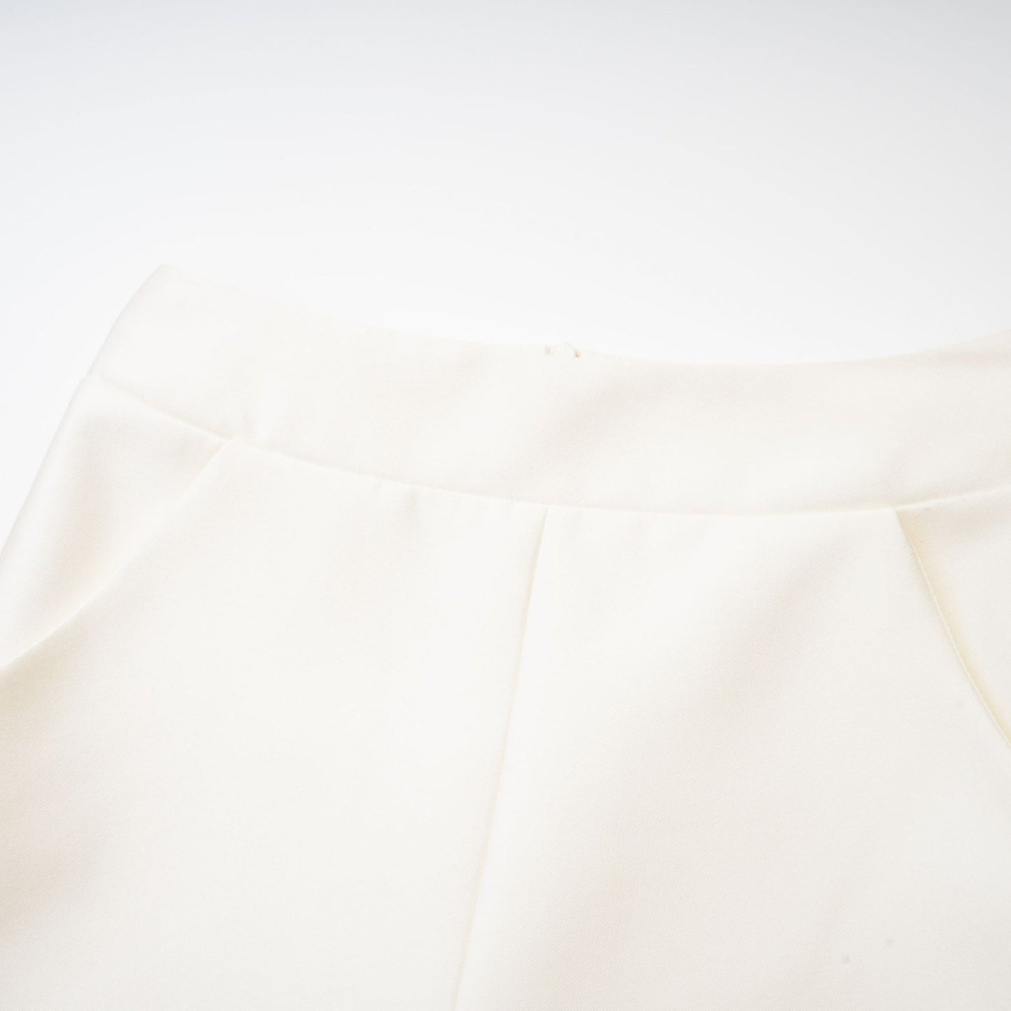 Young woman wearing a white sleeveless top and matching skirt set standing against a plain background