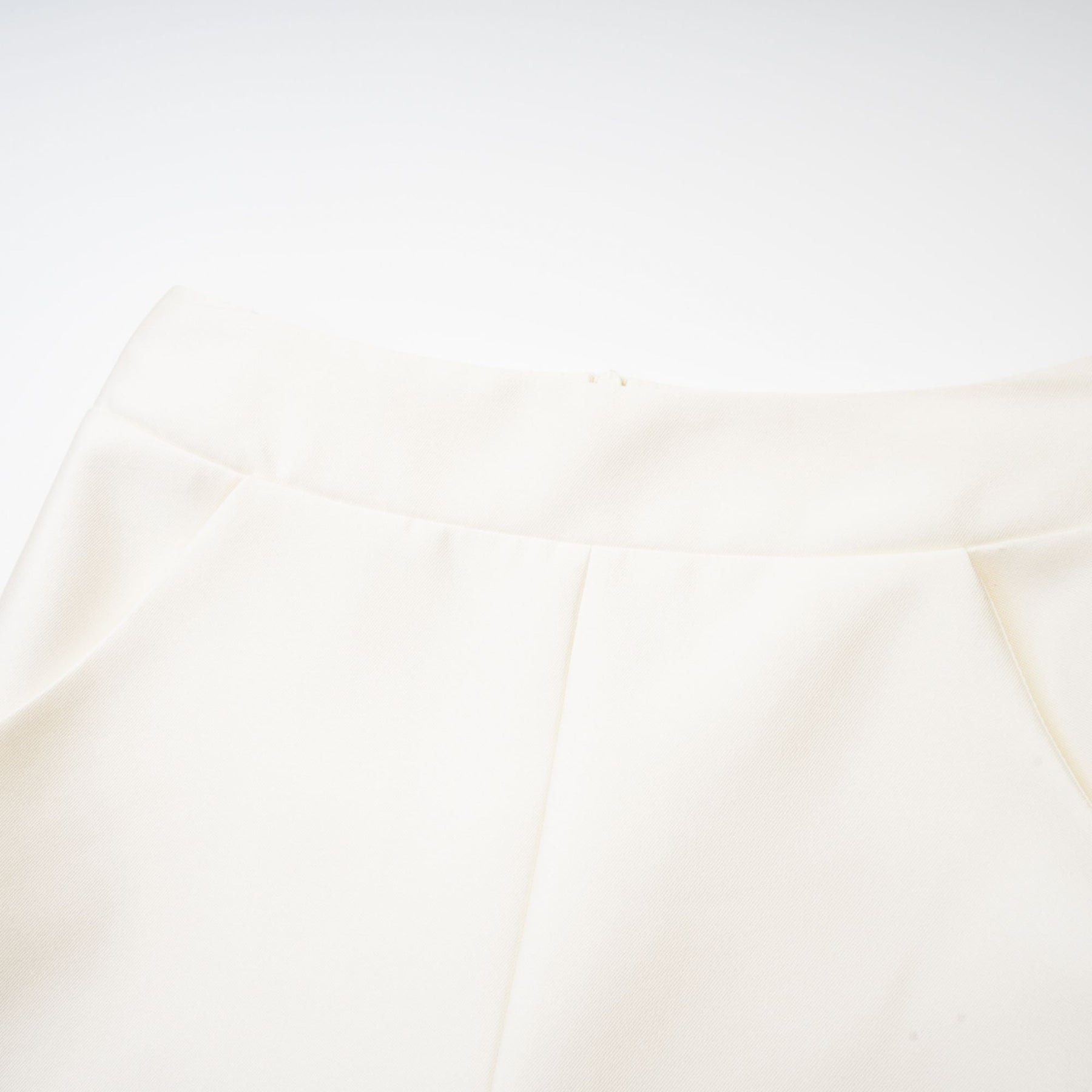 Young woman wearing a white sleeveless top and matching skirt set standing against a plain background